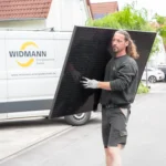 Unser Ablauf – Handwerker von Widmann Energietechnik mit schwarzem Solarmodul auf der Straße.