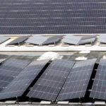 Reihen von aufgeständerten und flach verlegten Photovoltaik-Modulen auf dem grauen Flachdach eines großen Gebäudes.