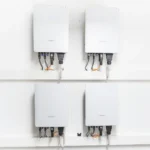 Vier Sungrow Wechselrichter sind sauber an einer weißen Wand montiert, Kabel führen unten heraus.