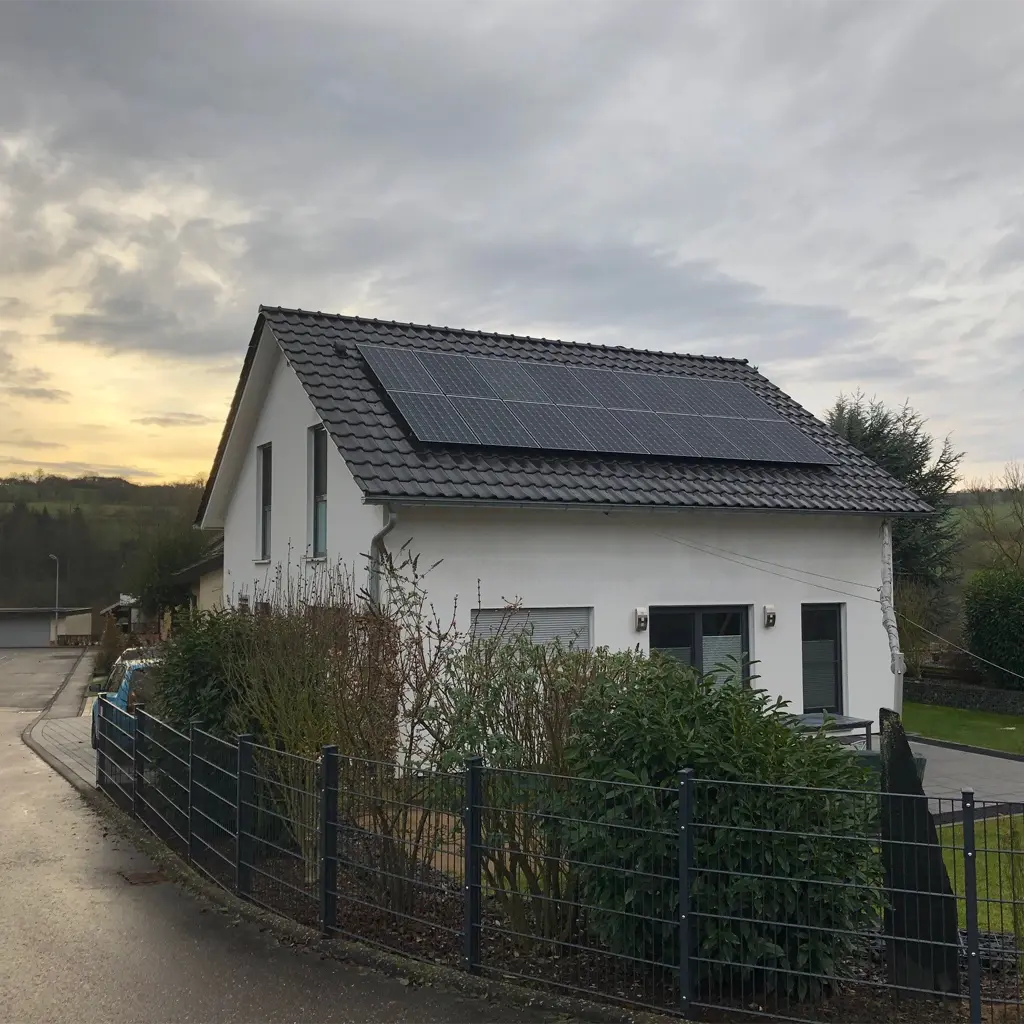 Photovoltaik Herbolzheim: Schwarze Solarmodule auf weißem Hausdach vor bewölktem Himmel.