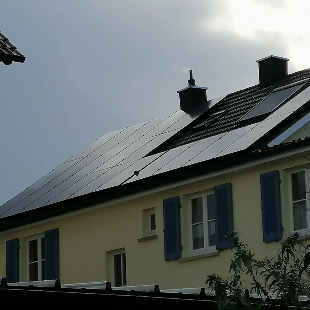 Photovoltaik Lauffen am Neckar: Schwarze Solaranlage auf gelbem Hausdach mit blauen Fensterläden.